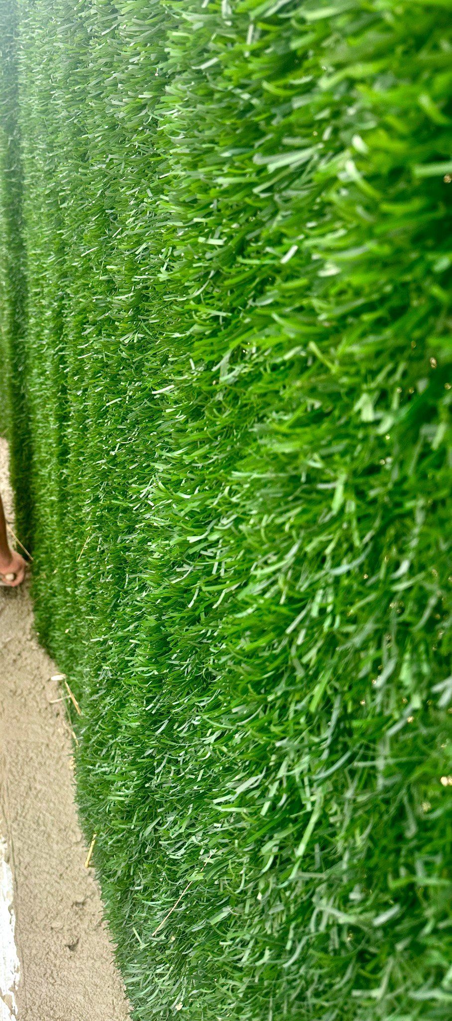 Primer plano de una pared de césped artificial de un verde vibrante. Un borde de arena la bordea.