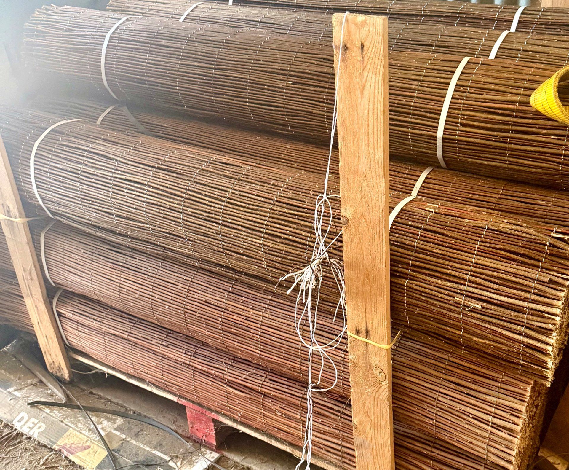 Esteras tejidas de color marrón apiladas sobre un palé, aseguradas con cordel y con una viga de soporte de madera.