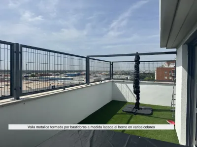Barandilla de metal en una terraza en la azotea con césped artificial, cielo azul y vistas a la ciudad.