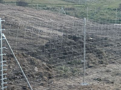 Una valla metálica rodea un campo arado, en un entorno rural.