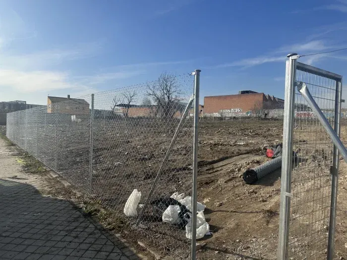 Una valla de alambre rodea un campo de tierra con un edificio de ladrillos al fondo.