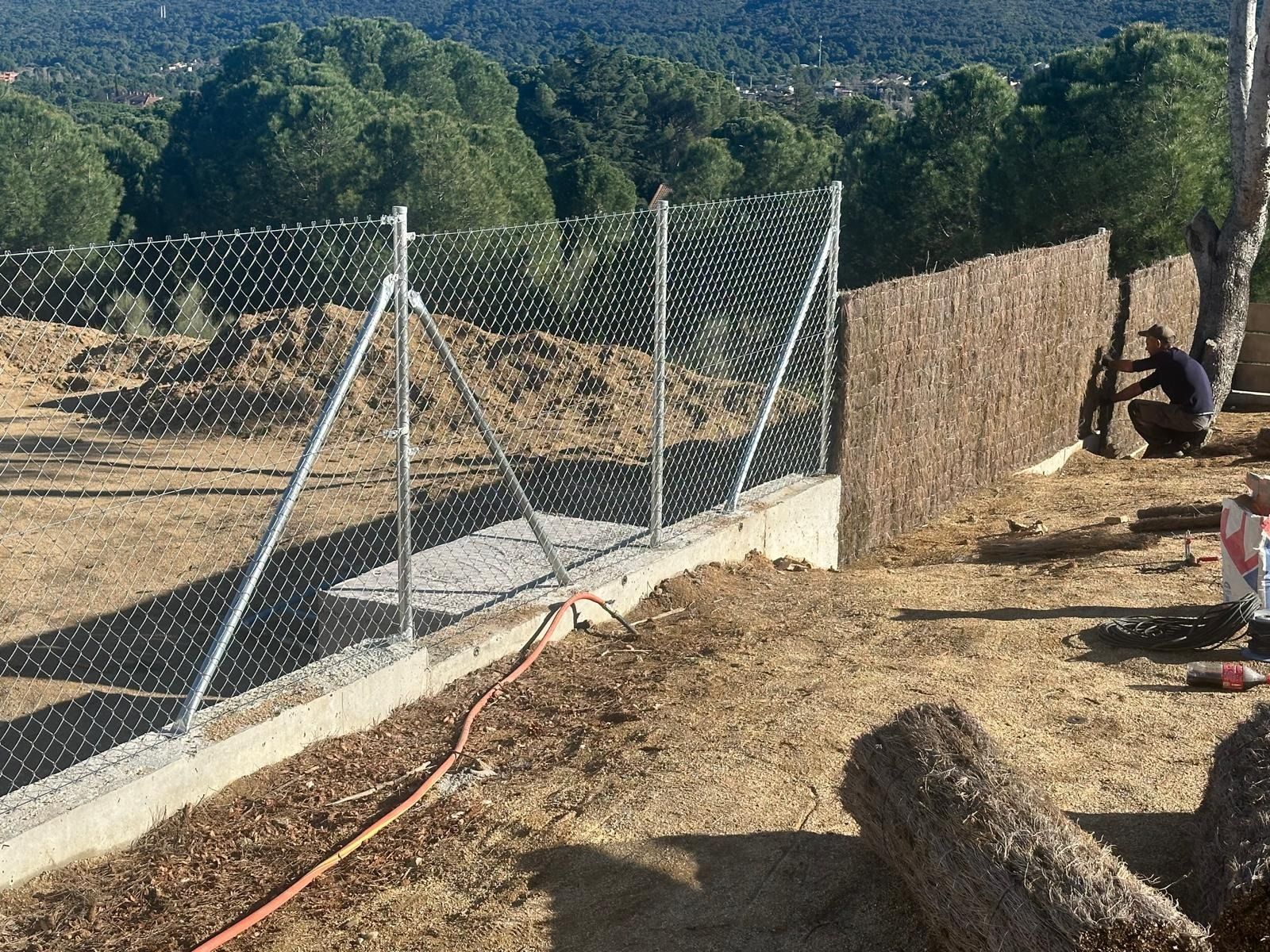 Cerca de alambre de cadena con pantalla de caña siendo instalada al aire libre por una persona en un entorno soleado.