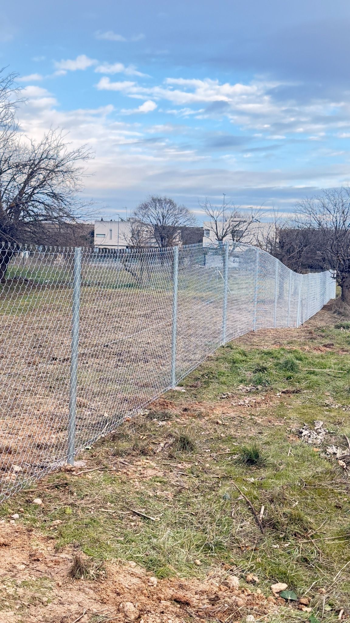 Valla de alambre en un campo con un cielo nublado al fondo, posiblemente en una zona suburbana.