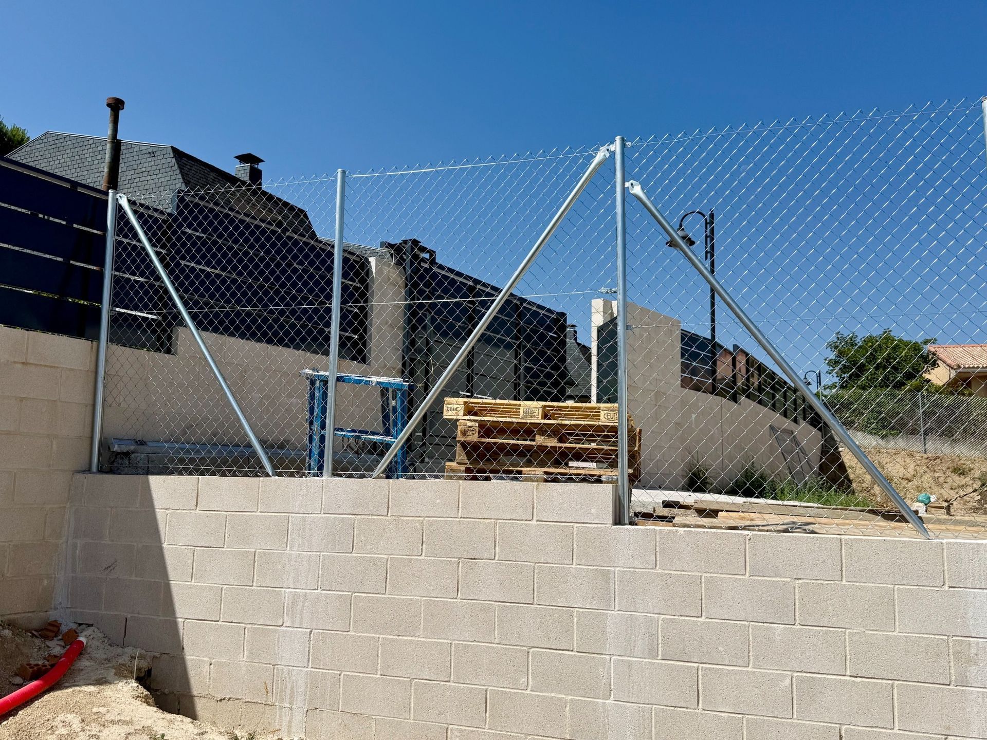 Construcción de una valla de alambre sobre un muro de bloques de hormigón; arriba hay un cielo azul.