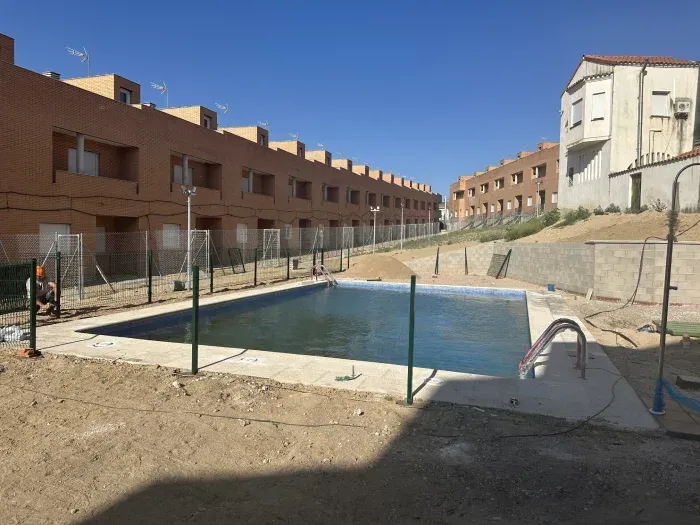 Una gran piscina está rodeada por una valla y edificios.