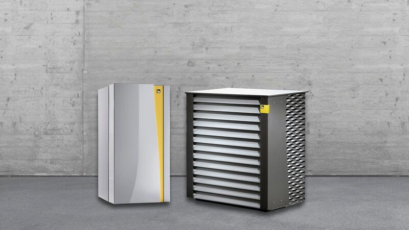 Zwei Industriemaschinen, eine geschlossen, die andere mit sichtbaren Lamellen, vor einer Betonwand.