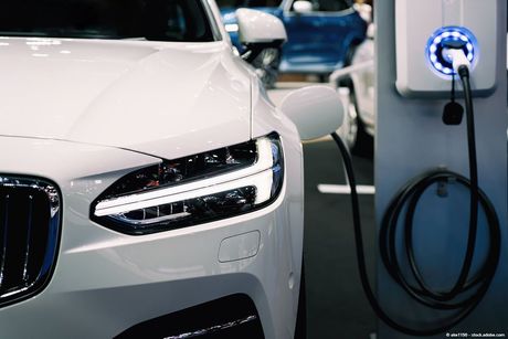 Ein weißes Elektroauto wird an einer Ladestation aufgeladen. Ein schwarzes Kabel ist am Auto angeschlossen.