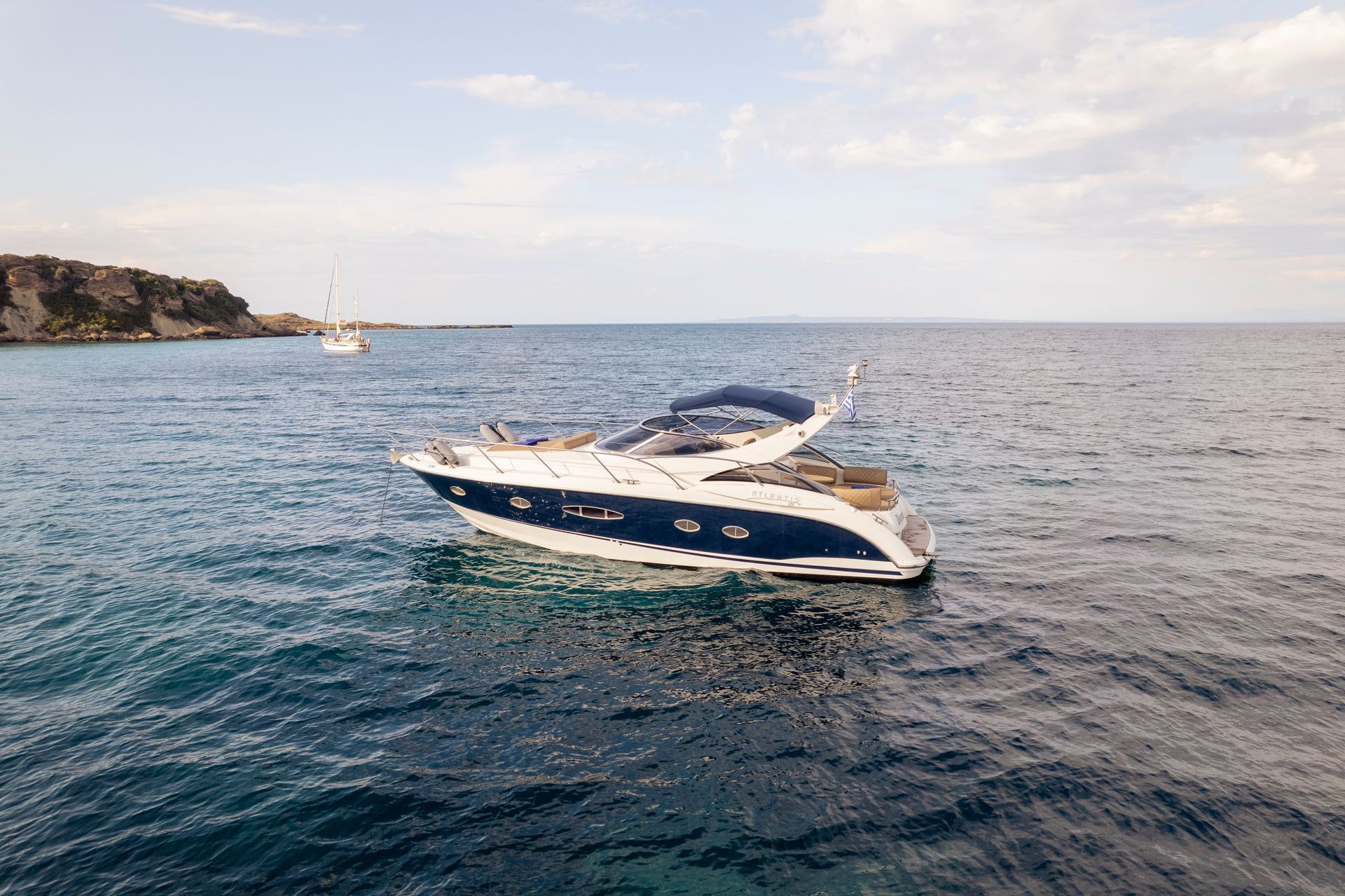 Blue-and-white motorboat cruising on choppy water near a rocky coastline under a partly cloudy sky