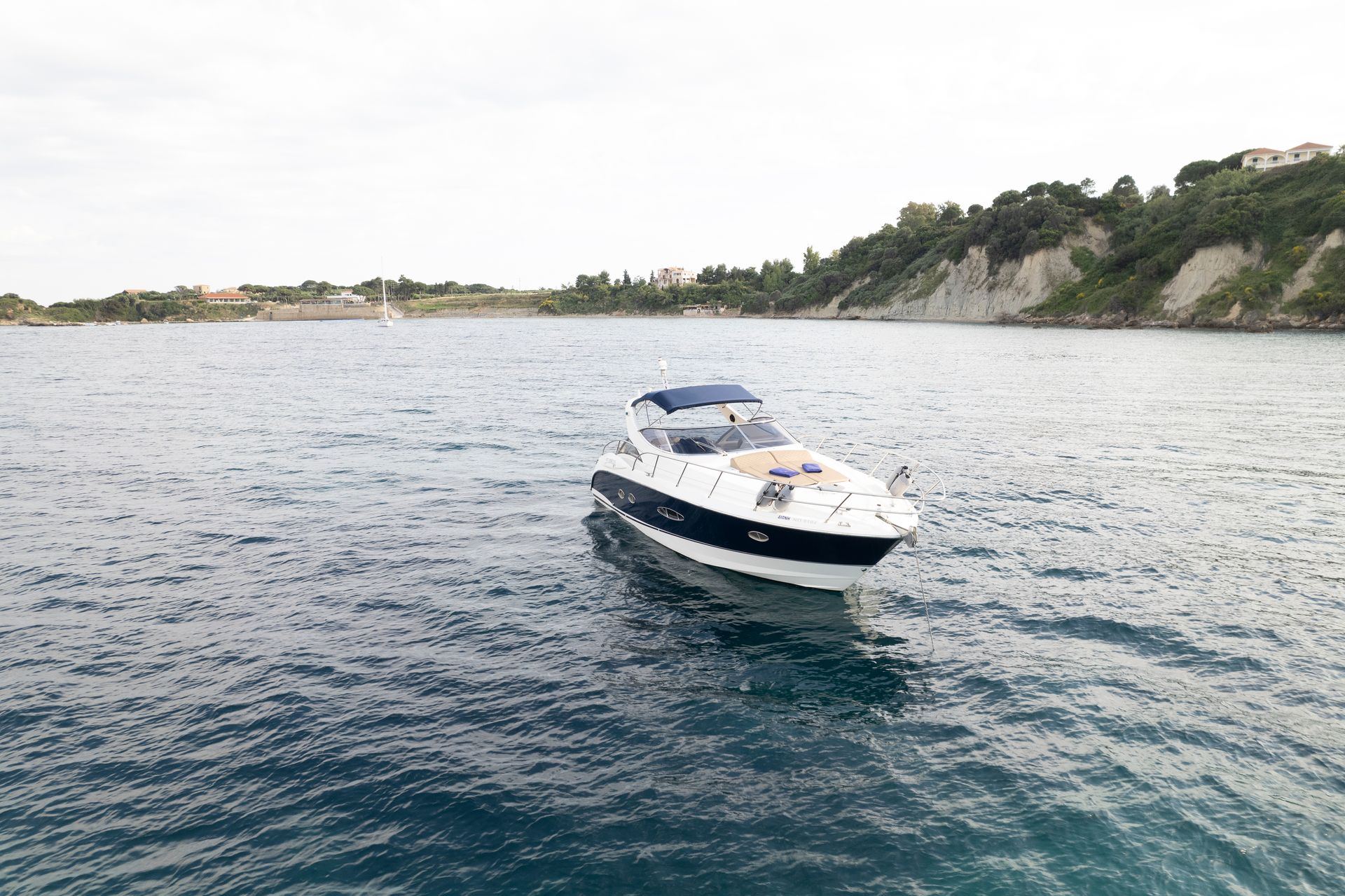 White motorboat floating on calm water near a rocky shoreline under a bright sky