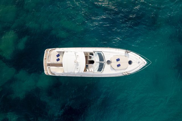 A white yacht cruising on turquoise ocean water, seen from above.