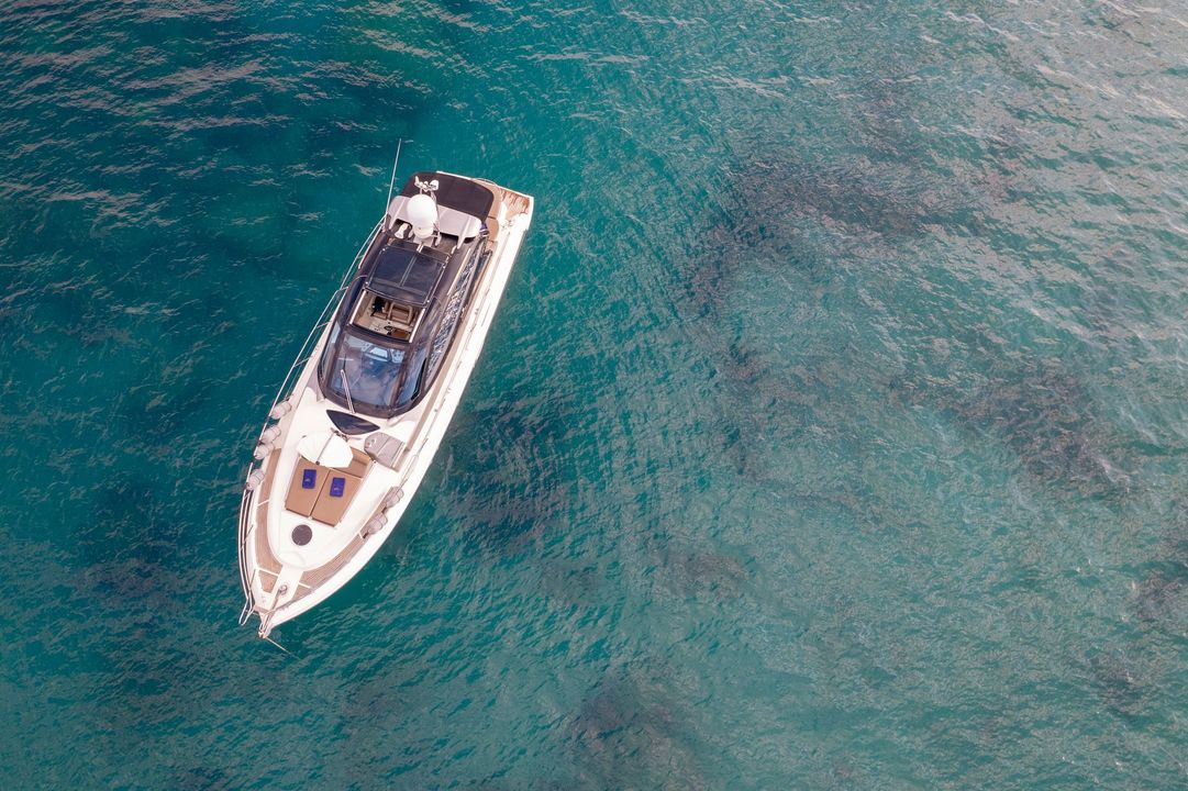 A white yacht floating on clear turquoise water, viewed from above.