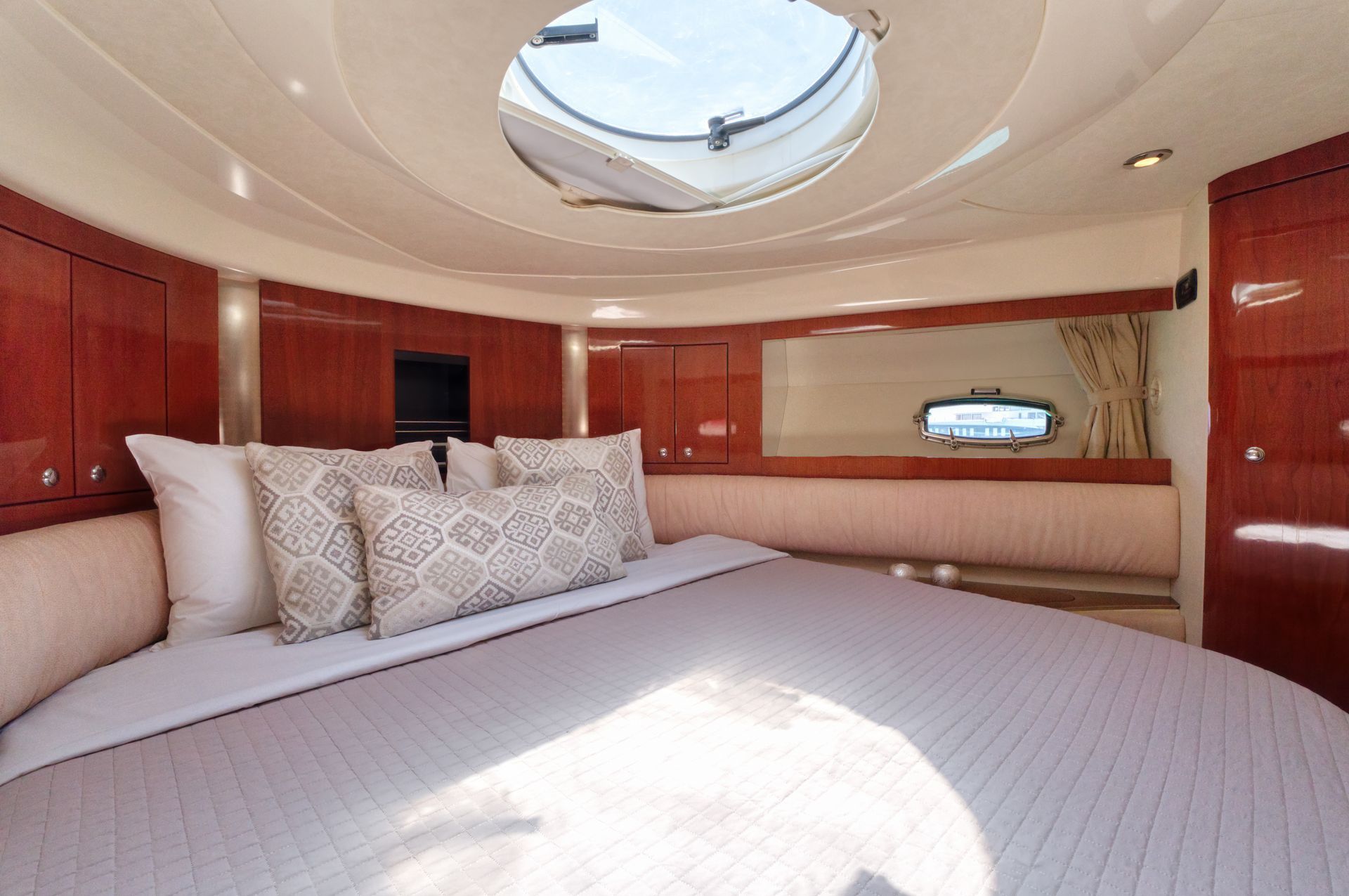 Luxury yacht cabin with a large bed, wood paneling, and a skylight above