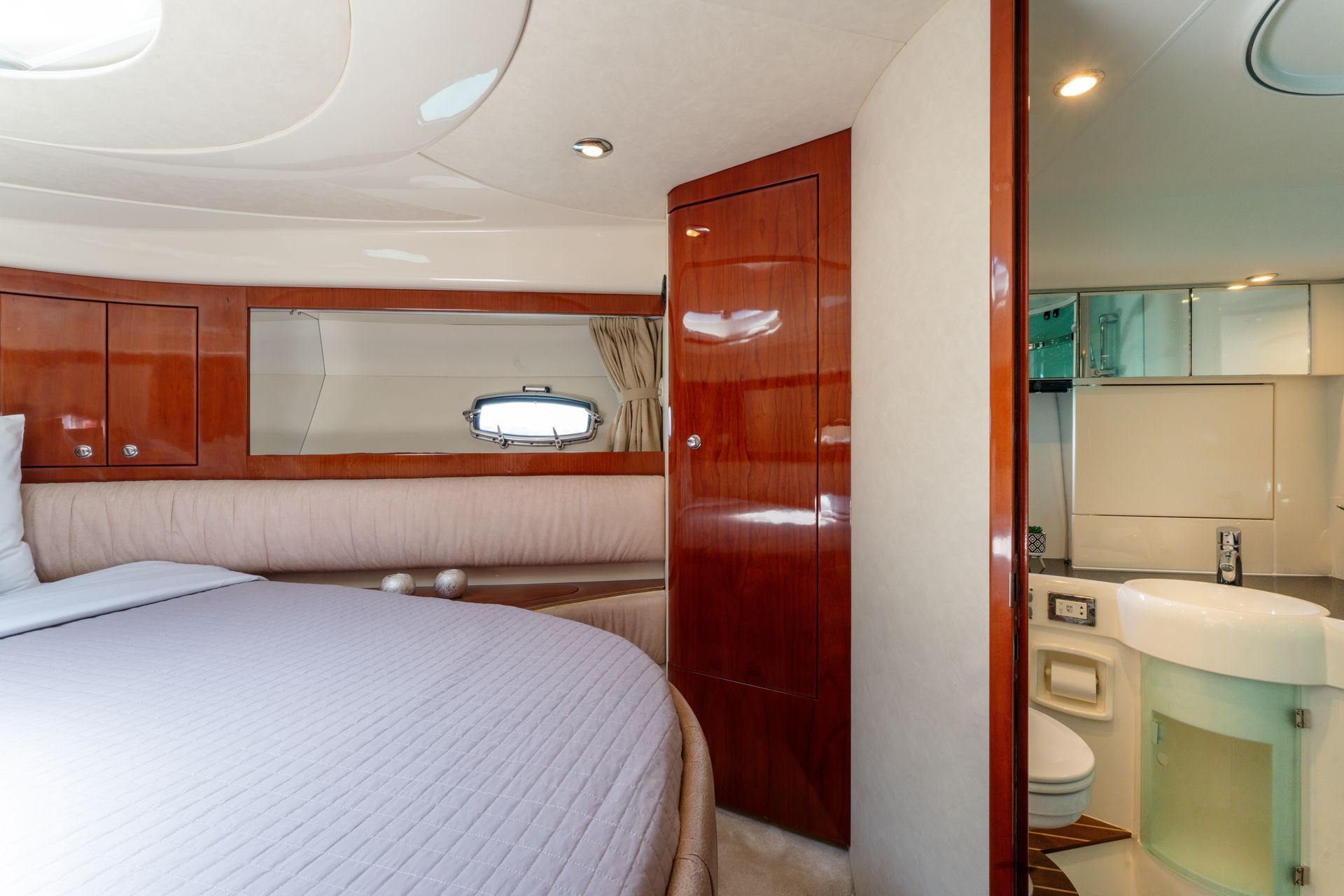 Luxurious yacht stateroom with bed and glossy wood cabinets, beside a small bathroom