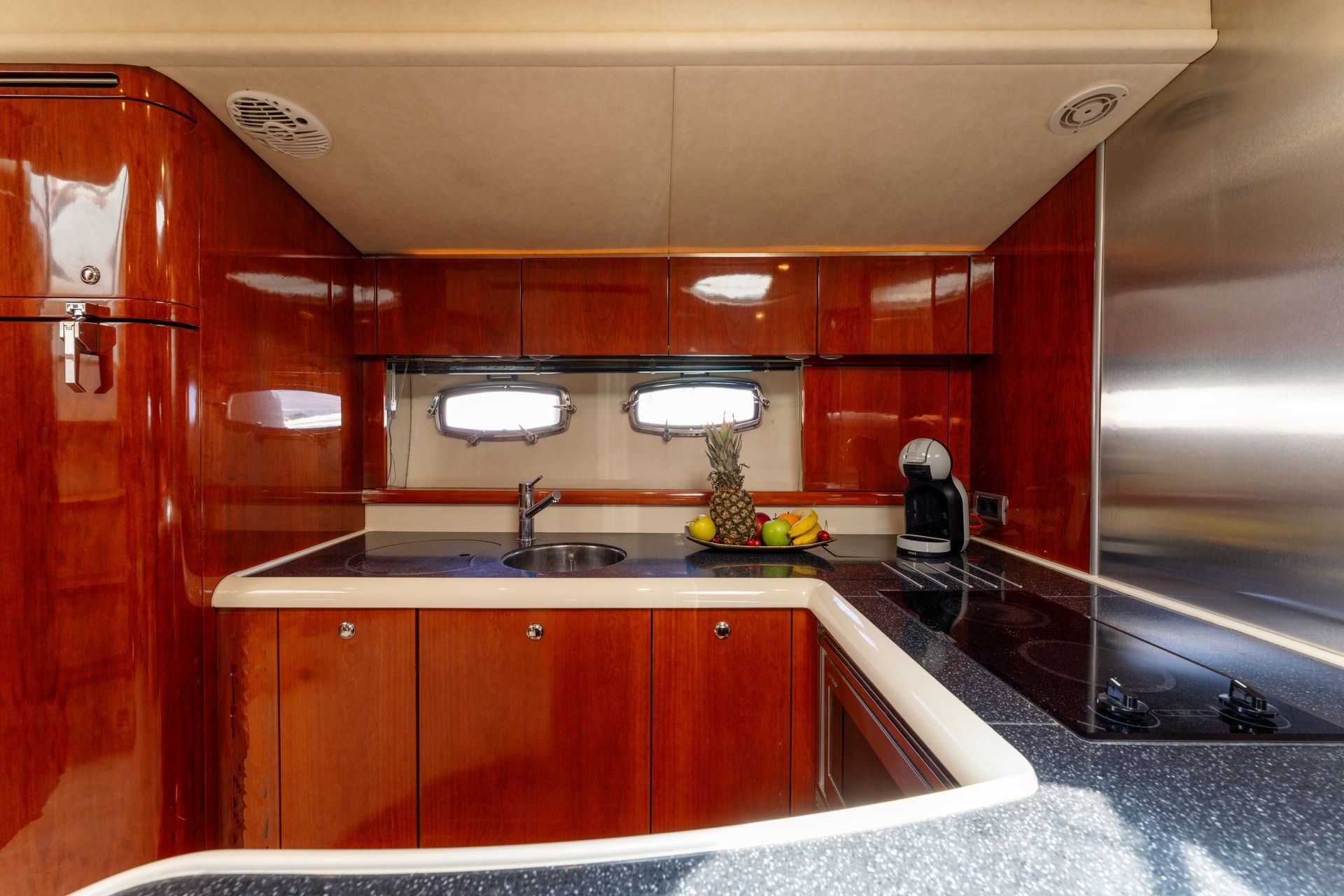 Compact modern kitchen with wood cabinets, stainless appliances, and a black-and-white counter under small windows