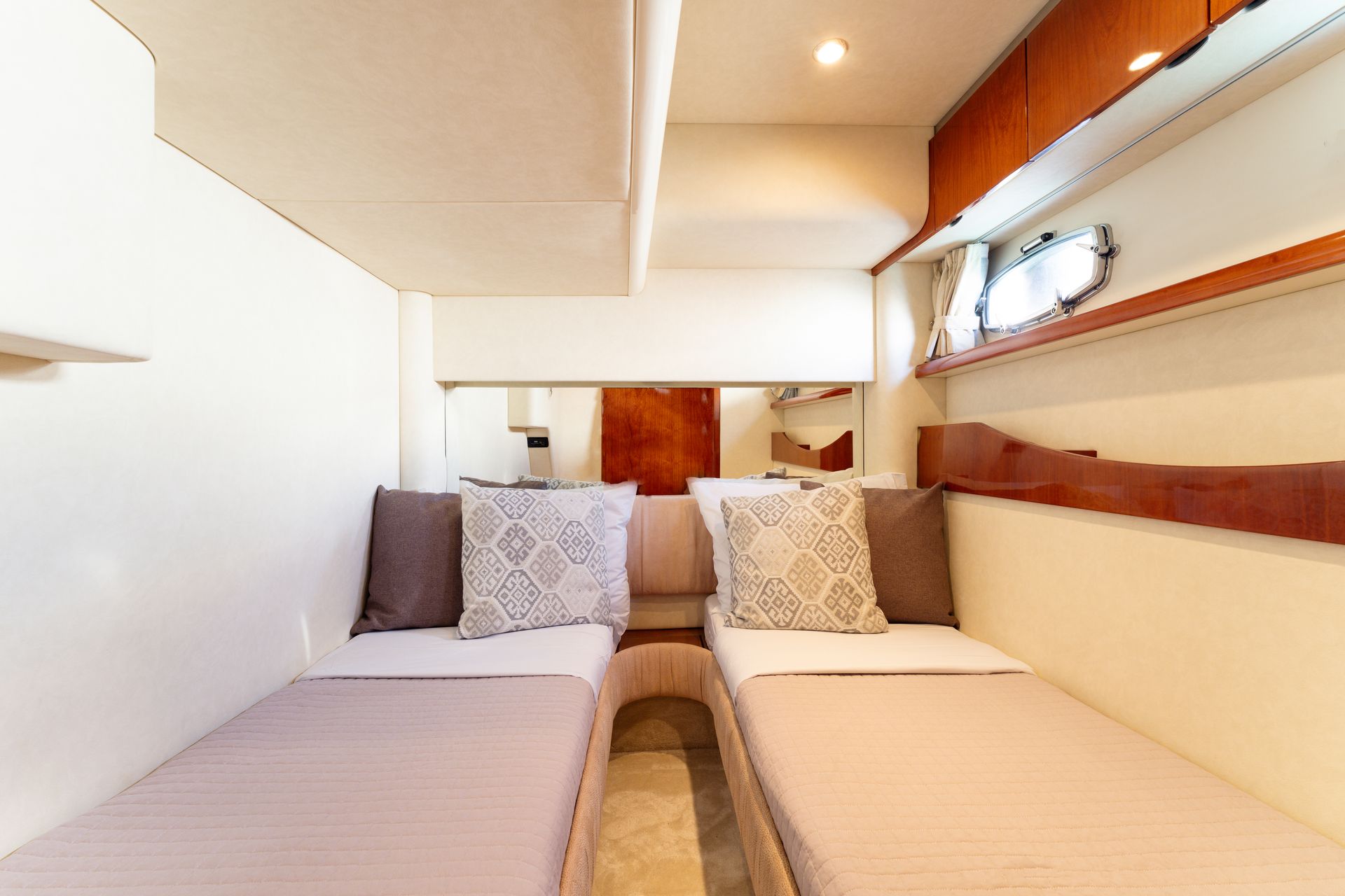 Narrow twin-bed cabin interior with beige bedding, pillows, and built-in shelves on both sides