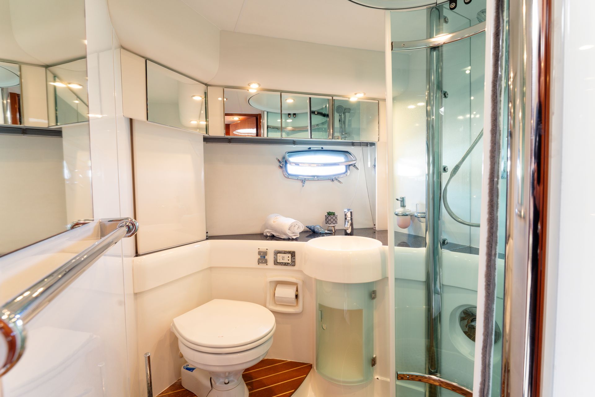 Bright yacht bathroom with white toilet, sink, and glass shower enclosure