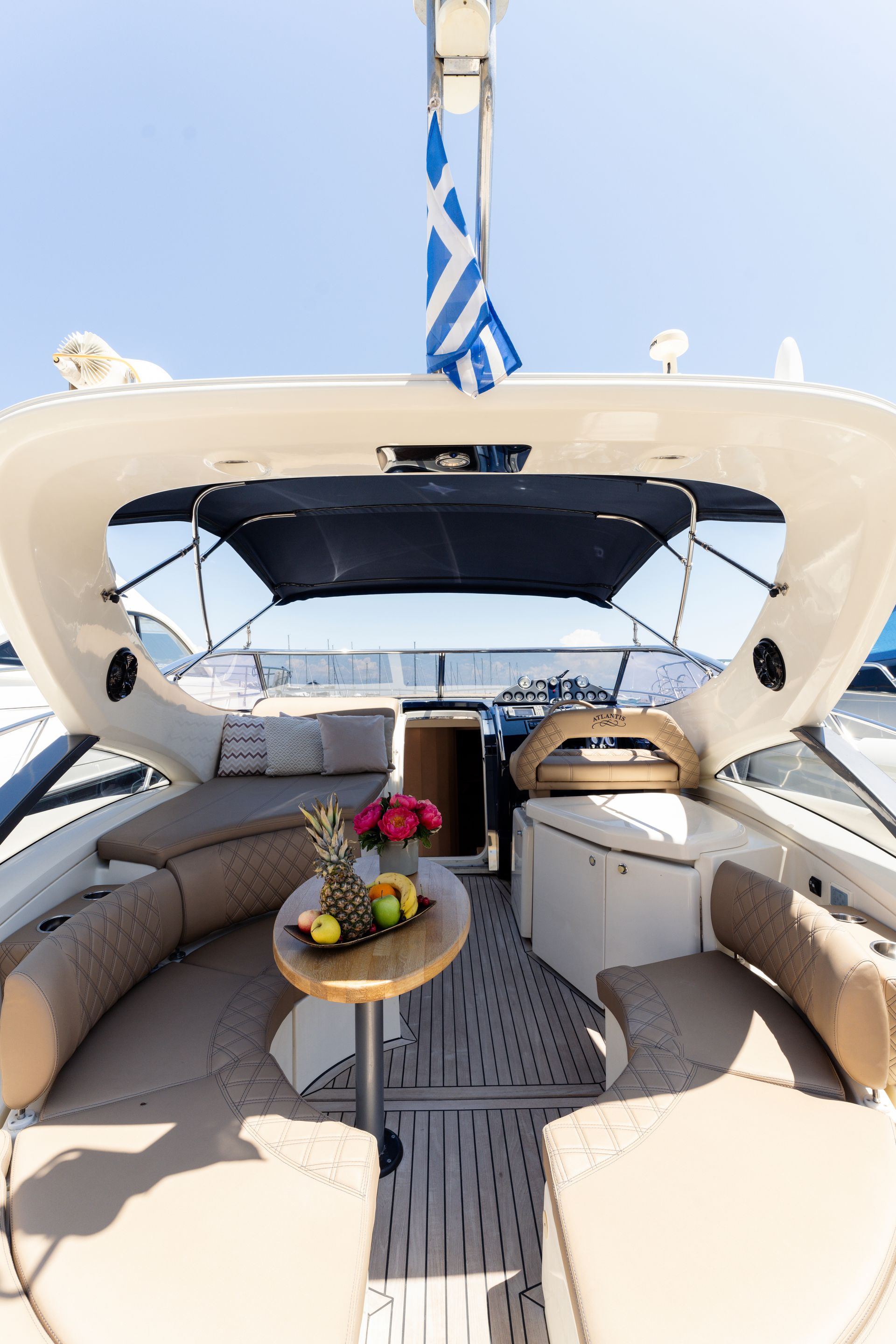 Luxury yacht cockpit with beige seating, a table of fruit, and a blue-and-white flag overhead