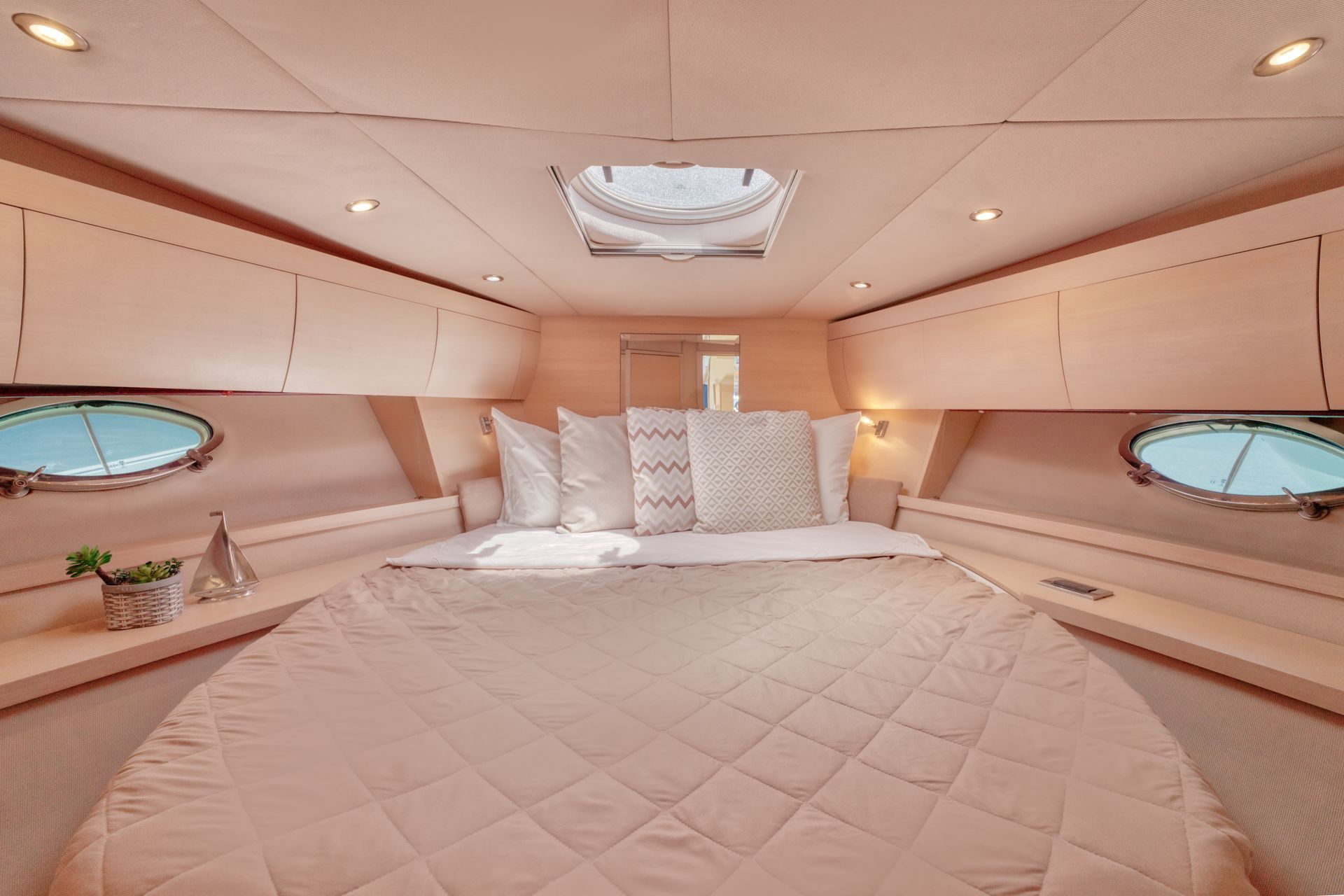 Luxurious beige yacht cabin with a large bed, oval windows, and soft recessed lighting