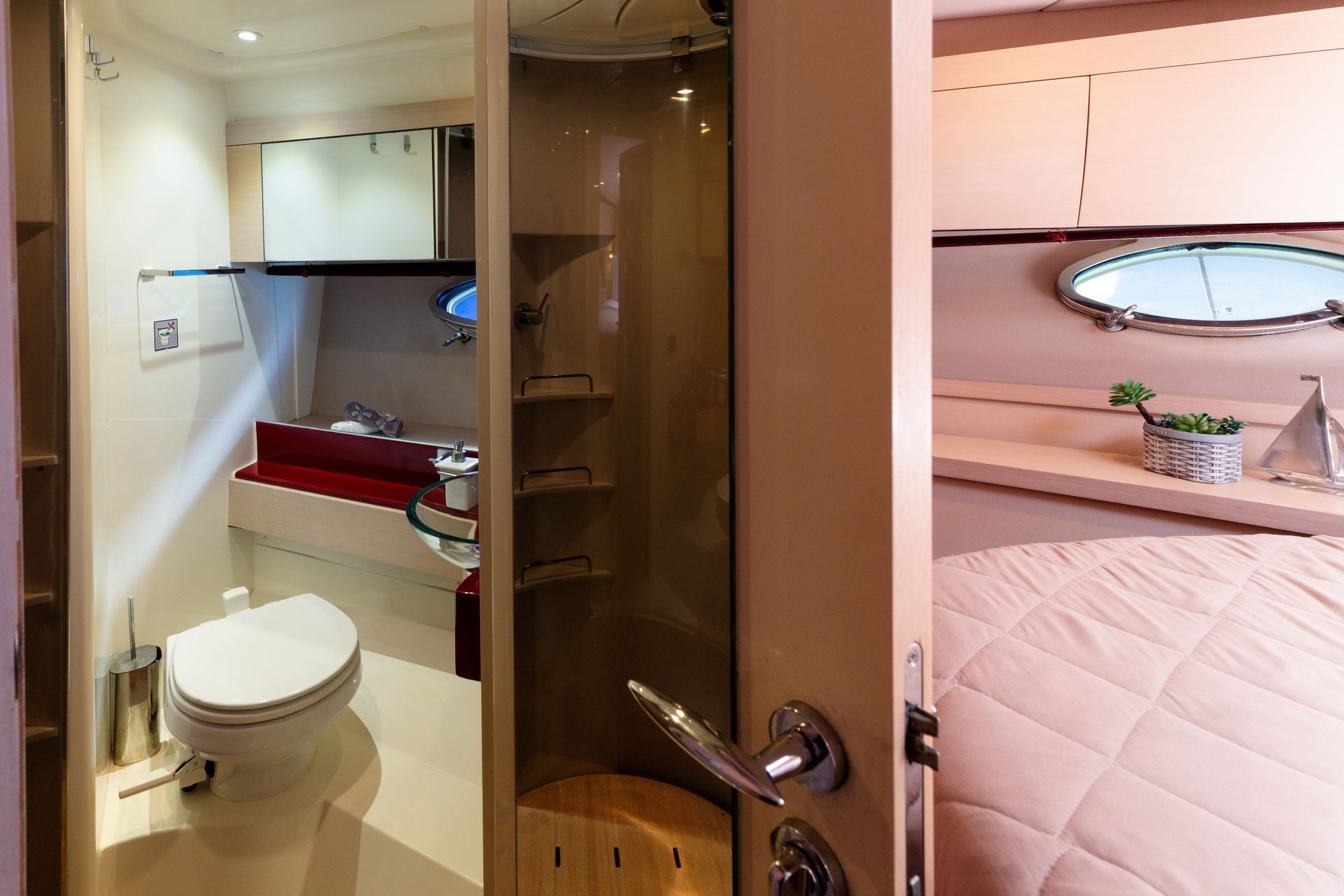Compact yacht cabin with bathroom and a bed, seen through an open door