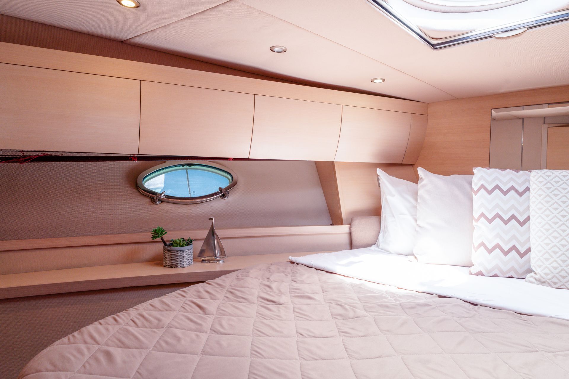 Cozy yacht cabin with white bedding, wood paneling, and a small oval porthole window.