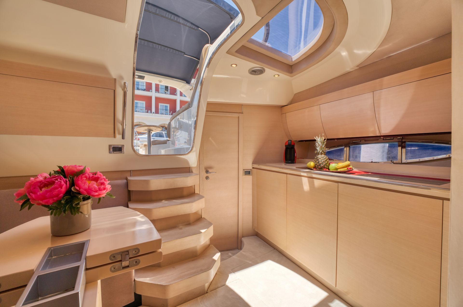 Bright boat cabin with steps, beige cabinetry, skylight, and a vase of pink flowers by the table