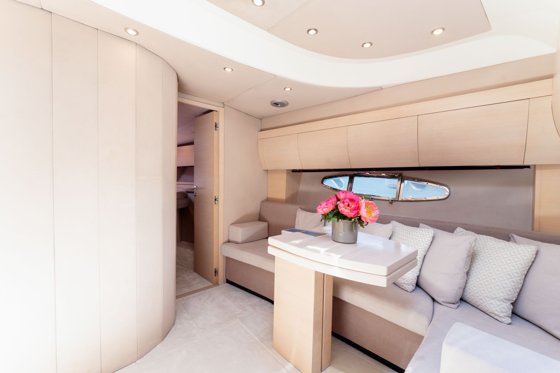 Compact luxury cabin with cream seating, built-in storage, and a flower arrangement by a window seat.