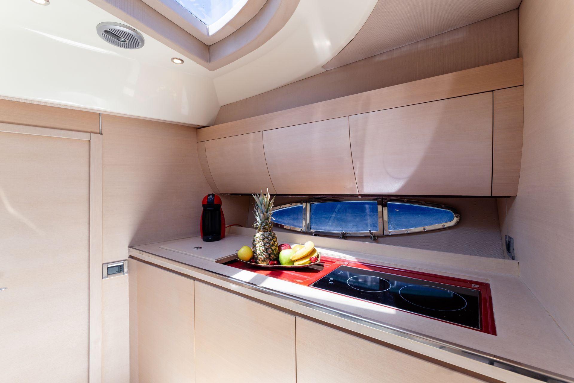 Compact yacht galley with beige cabinets, countertop decor, and oval porthole window at sea.
