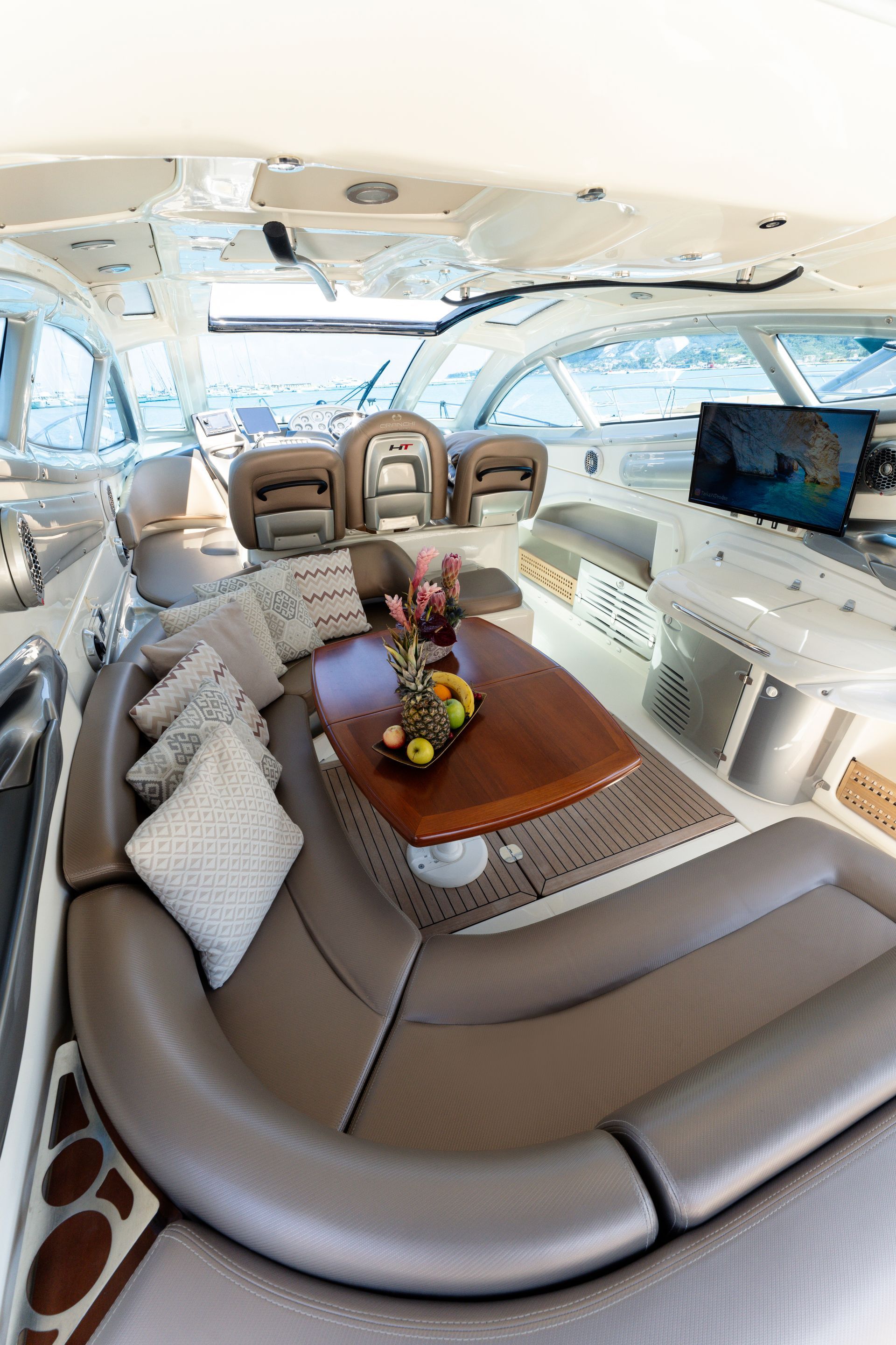 Luxury yacht salon with beige seating, wooden table, and TV by bright windows