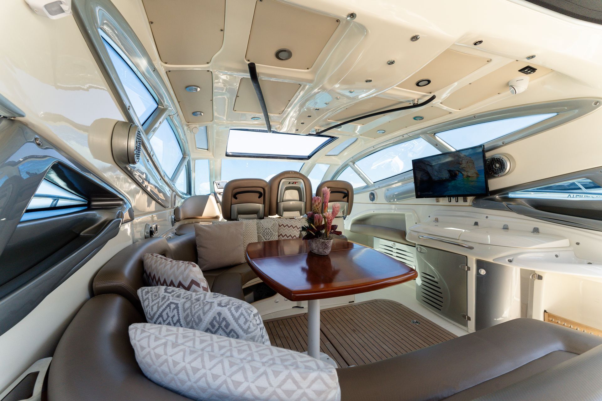Luxurious yacht cabin with beige seating, wooden table, and large windows overlooking the water