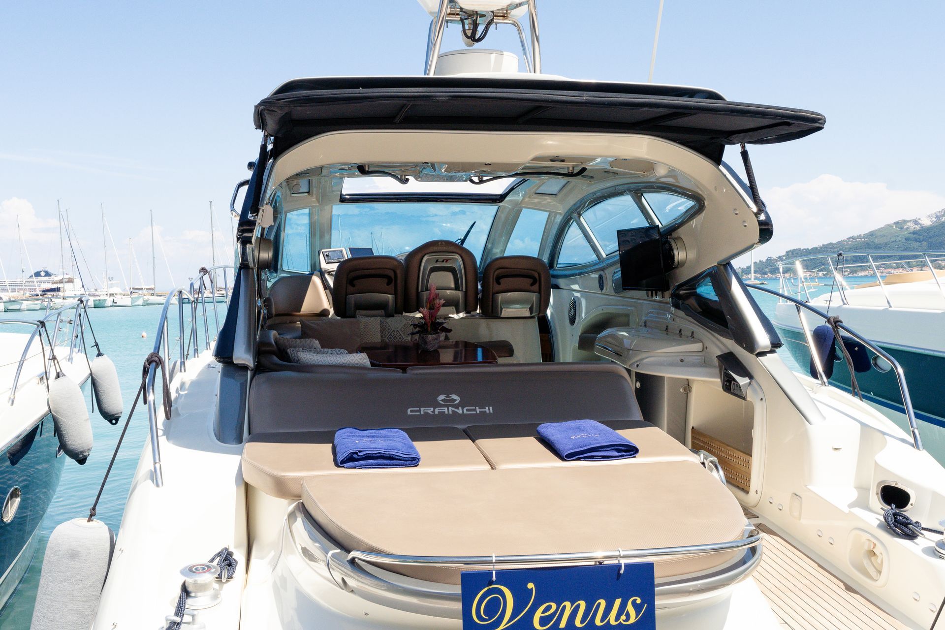 Luxury yacht cockpit and sun deck with beige seating and blue towels at a marina, named Venus