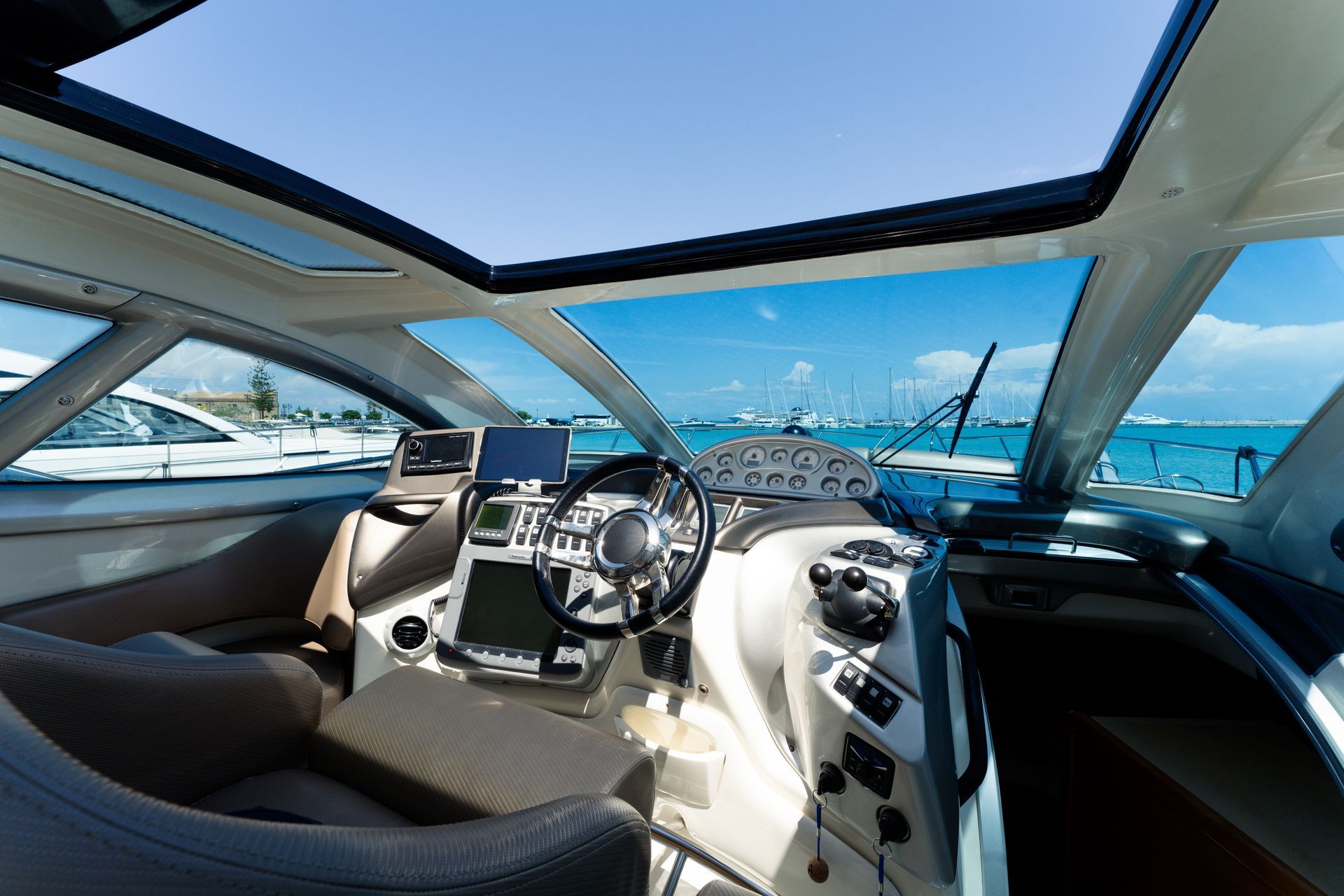Luxury boat cockpit with cream seats and steering wheel, overlooking a bright blue marina
