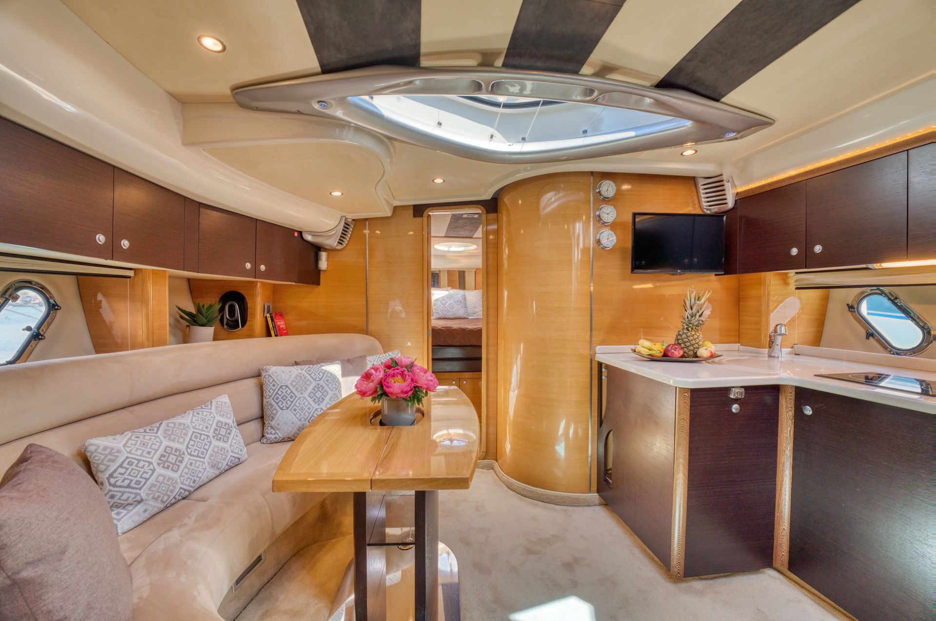 Luxurious yacht salon with beige seating, wood cabinetry, a small table, and a compact kitchenette