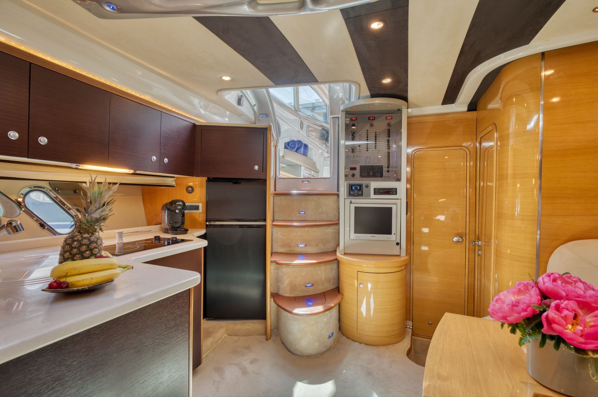 Compact luxury kitchen with curved wood cabinetry, countertop, and built-in appliances under warm lighting