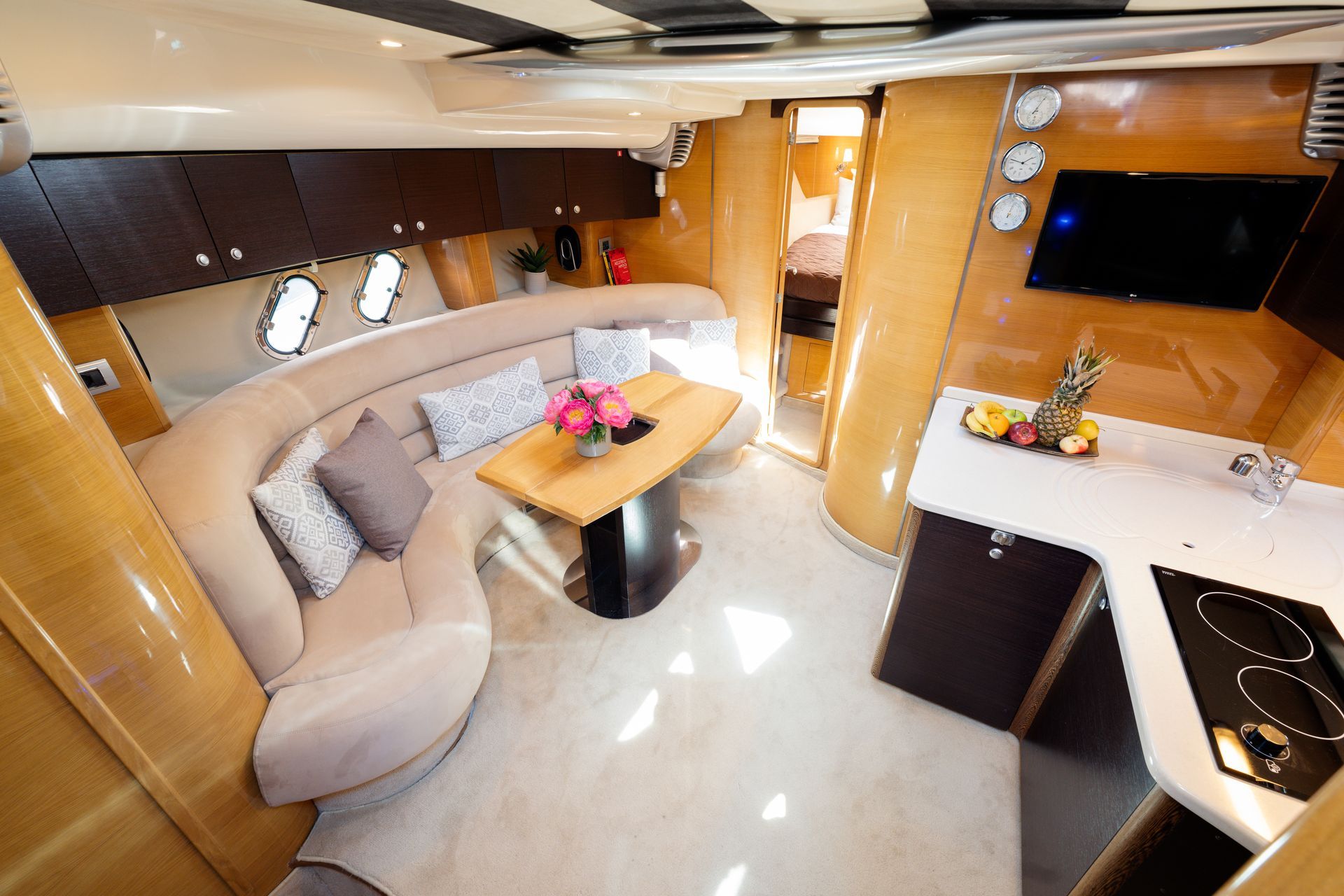 Luxury yacht salon with beige seating, wooden finishes, coffee table, and compact kitchen area