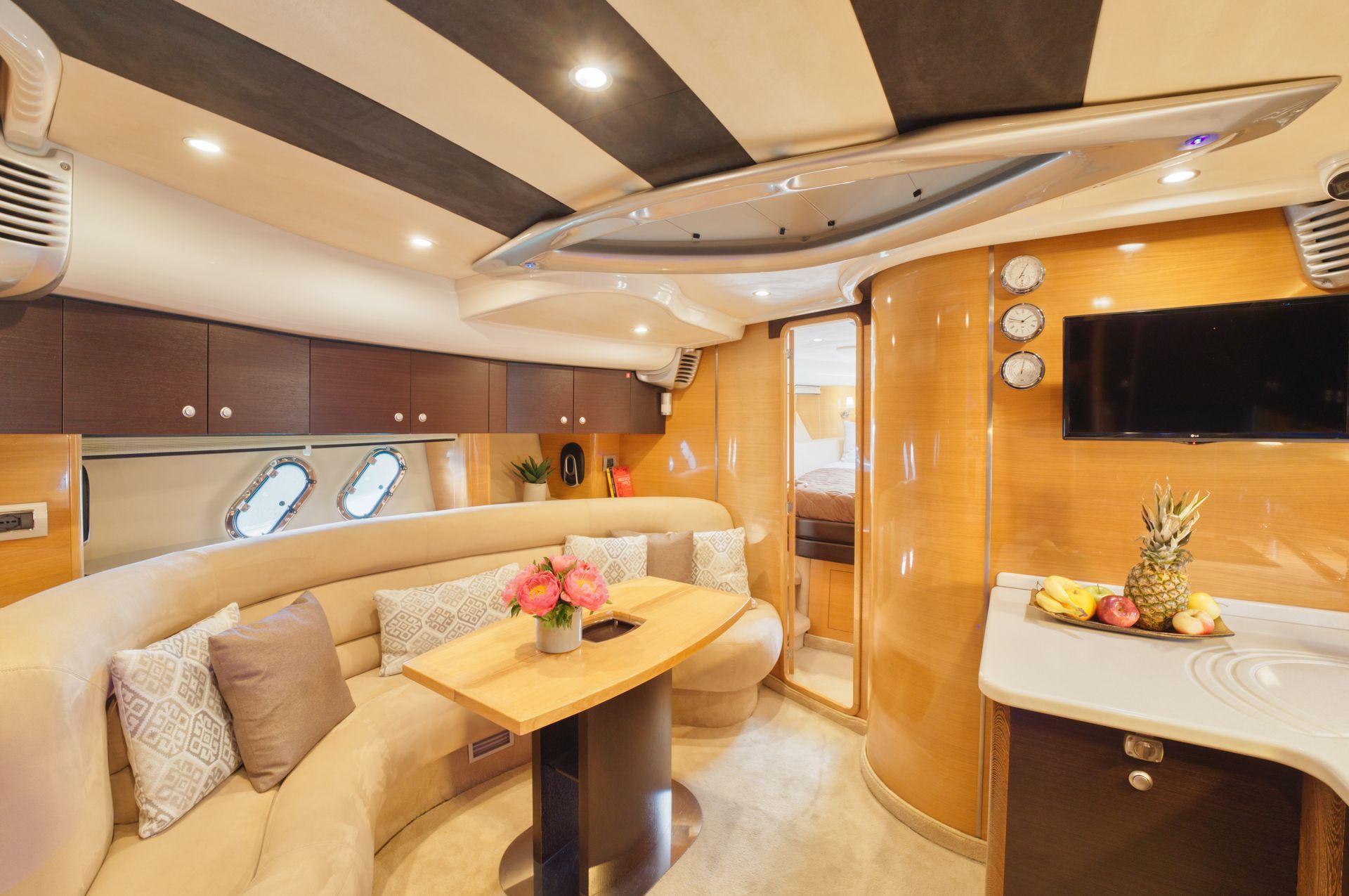 Luxurious yacht salon with cream seating, wood accents, table, and wall-mounted TV