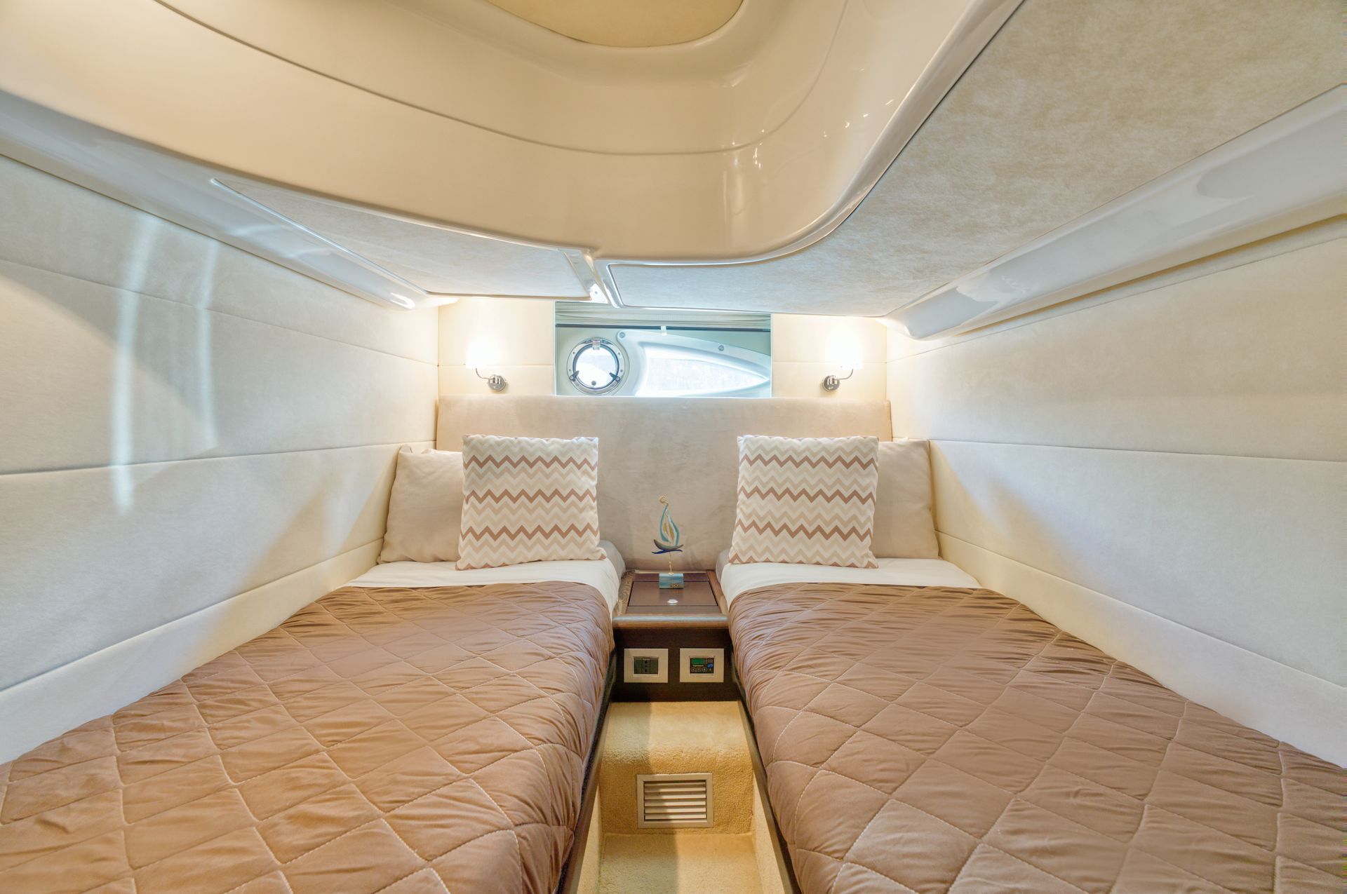 Small cabin with two tan beds, white walls, and a central aisle beneath a curved ceiling.