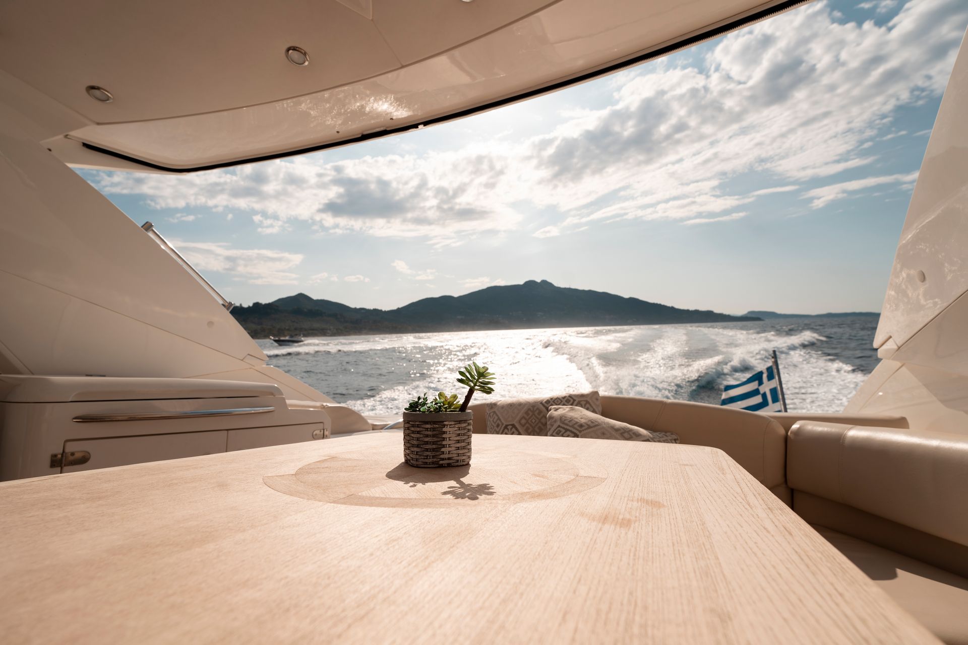 Yacht deck with a table, potted plant, and sunlit ocean view toward distant mountains