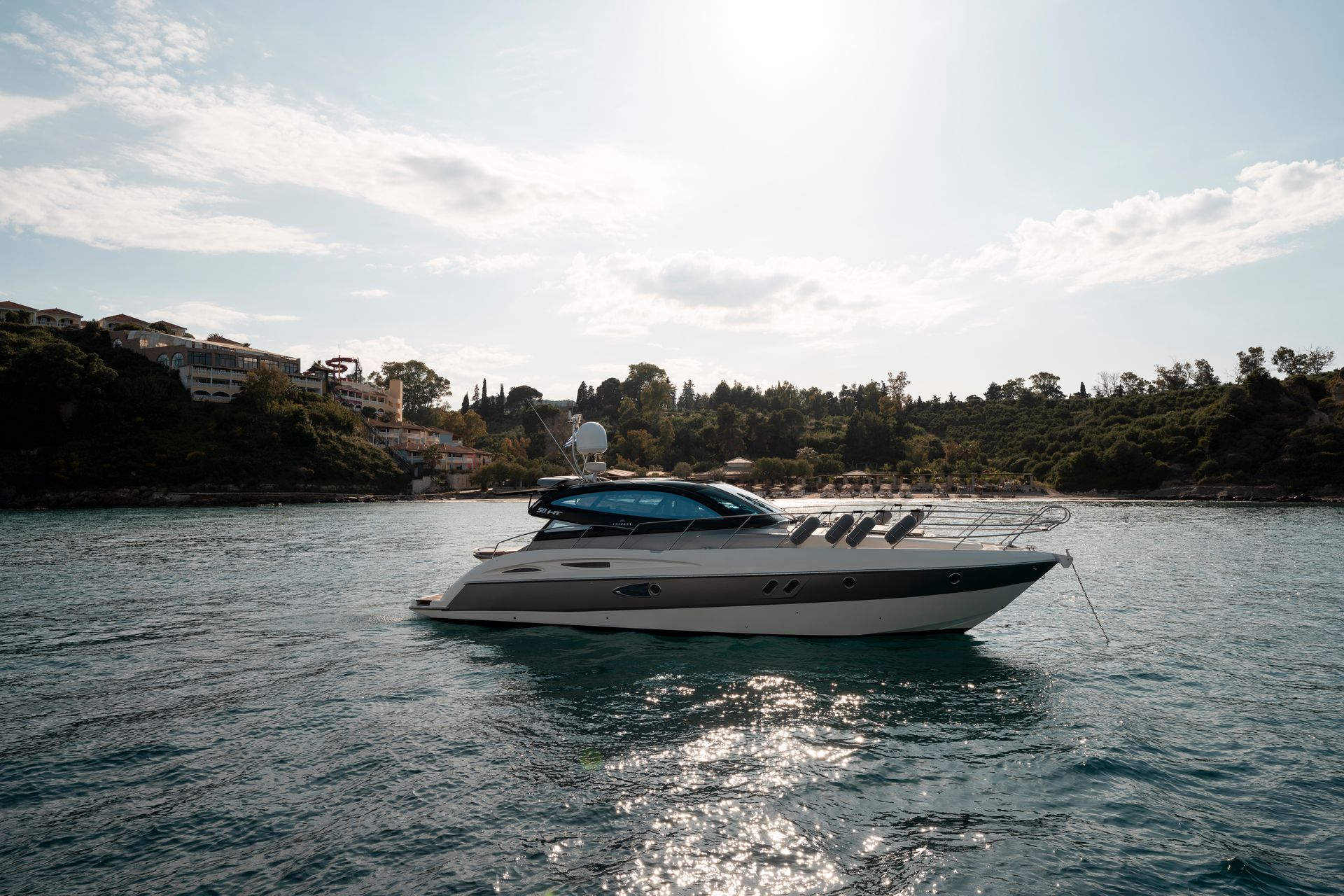 White yacht cruising on sparkling water near a wooded shoreline under a partly cloudy sky