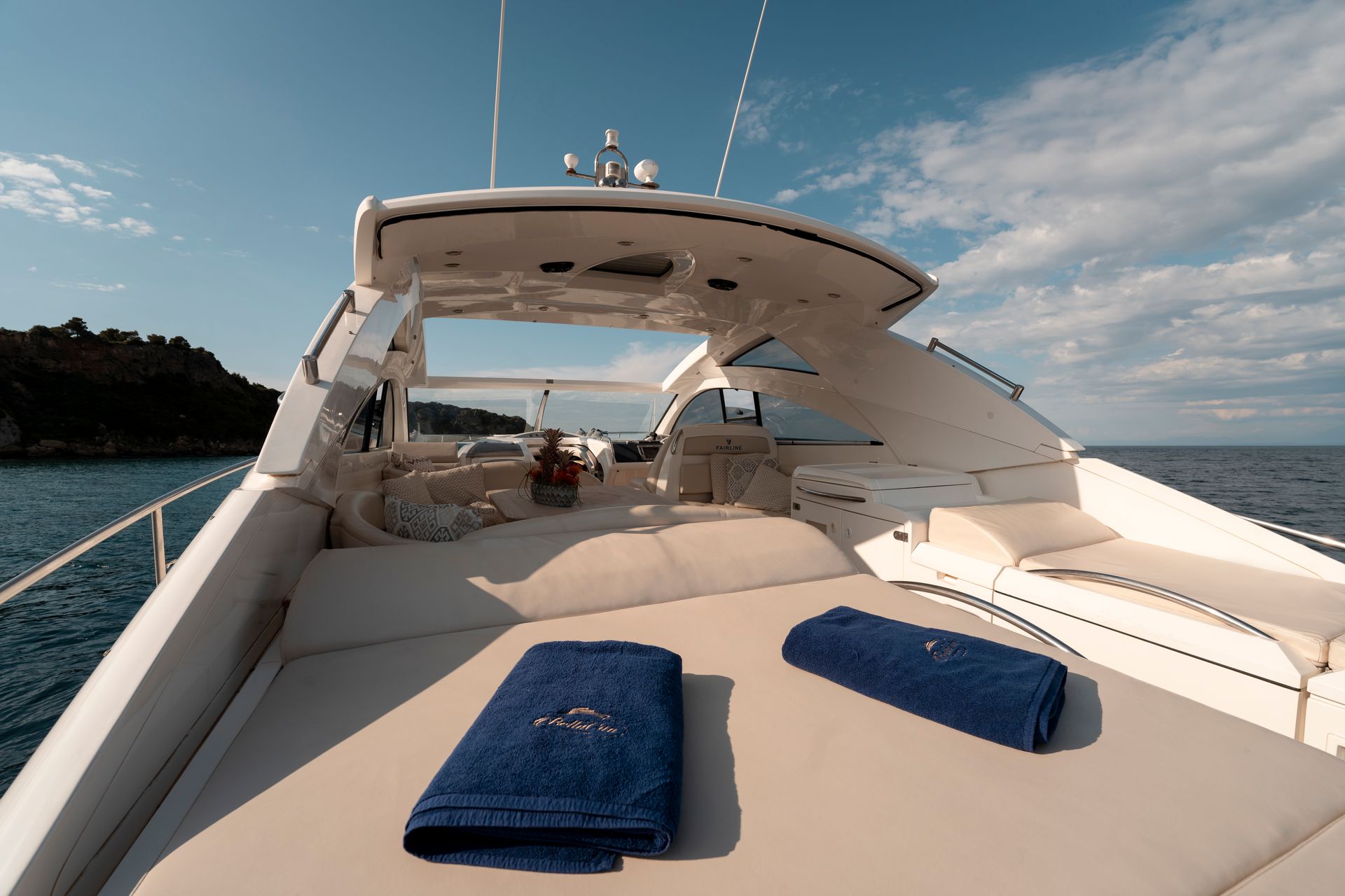 Luxury yacht deck with sun loungers and blue towels on a calm sea under a partly cloudy sky
