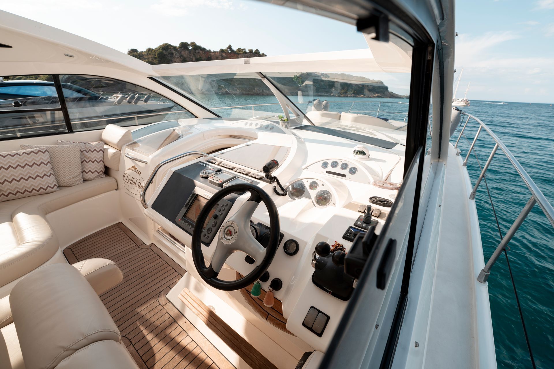 Luxury yacht cockpit with beige seats, steering wheel, and open view of the ocean and coastline