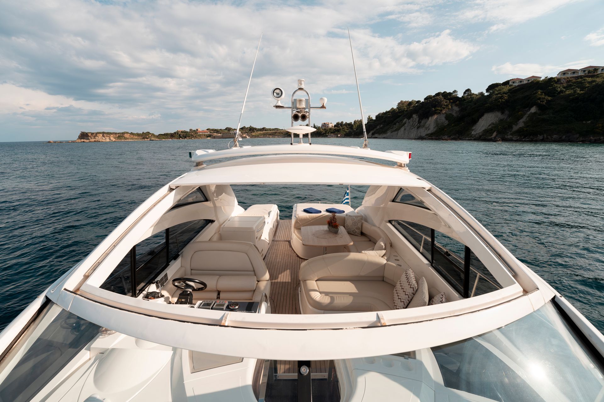 Luxury motor yacht cruising on calm water under a cloudy sky, with beige seating and coastal cliffs ahead