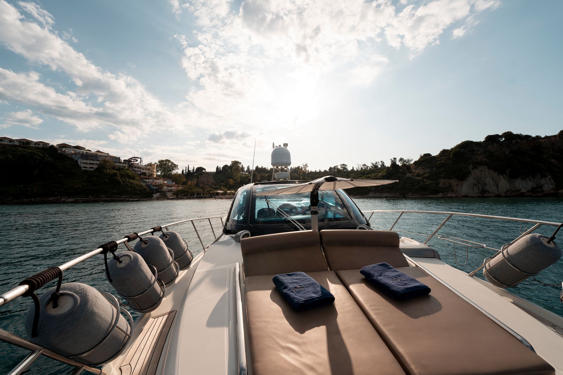 Motorboat cruising on blue water toward a sunny harbor, with tan sun loungers on deck