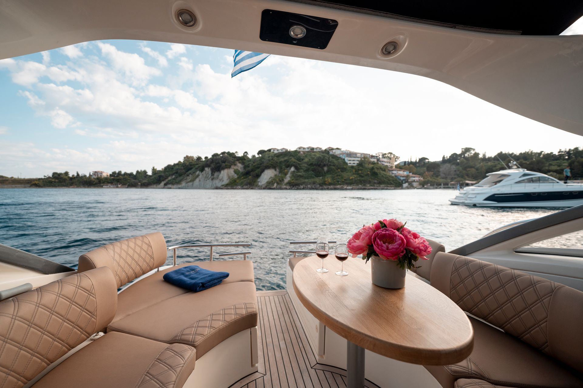 Luxury boat cockpit with tan seats, small table of pink flowers, and a view of water and a rocky shoreline