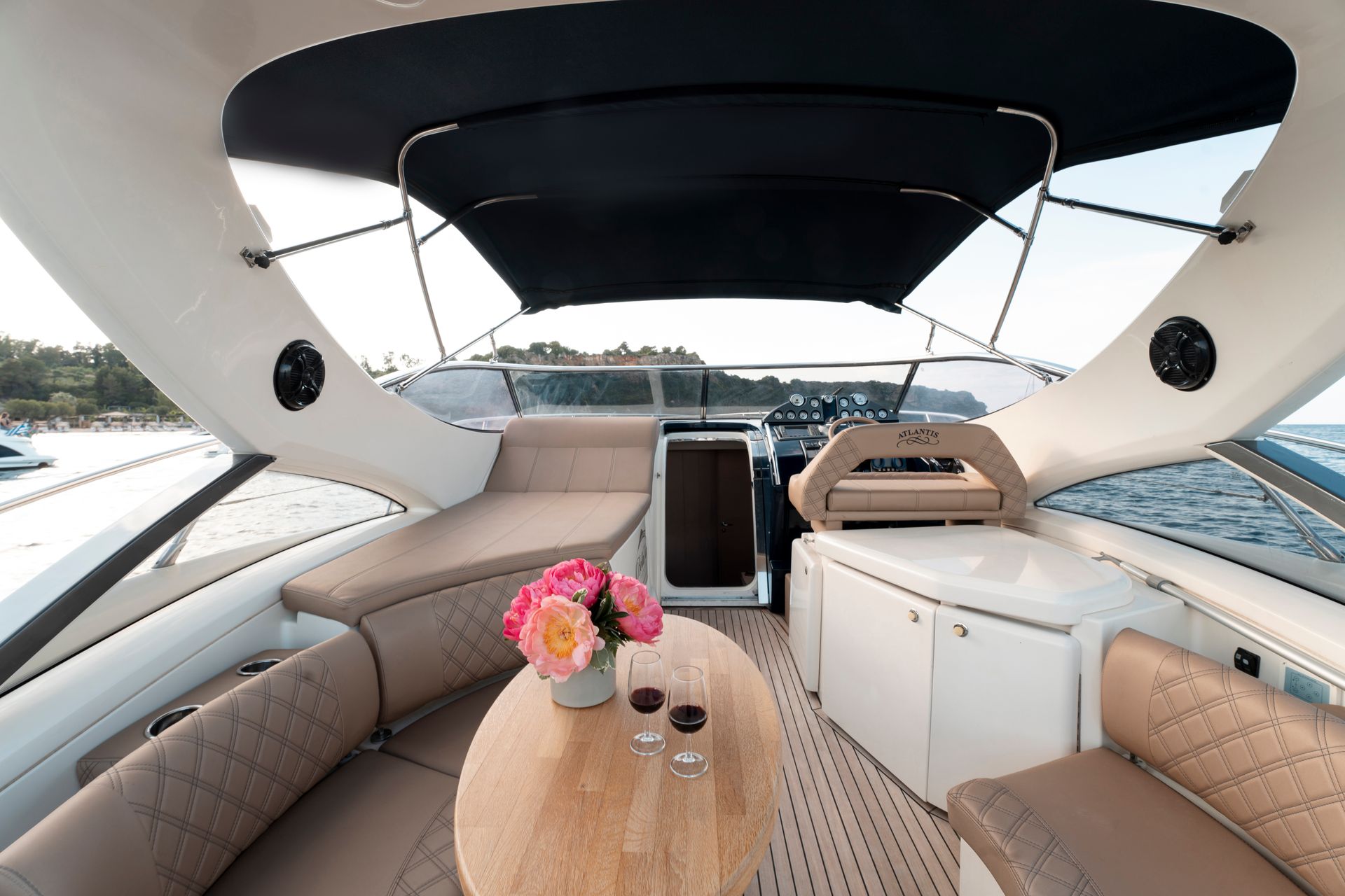 Boat cabin seating area with tan benches, small table, flowers, and black canopy on the water