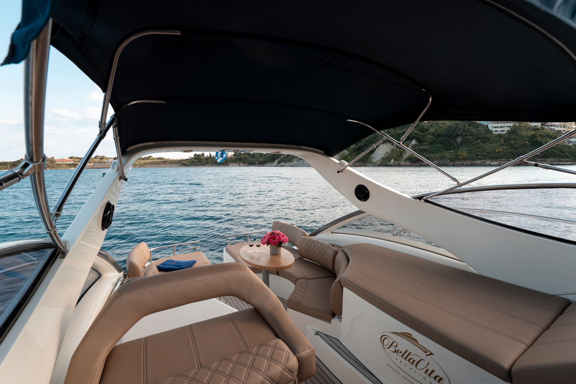 Boat cabin with beige seating and a black canopy, overlooking a calm blue bay and distant shoreline.