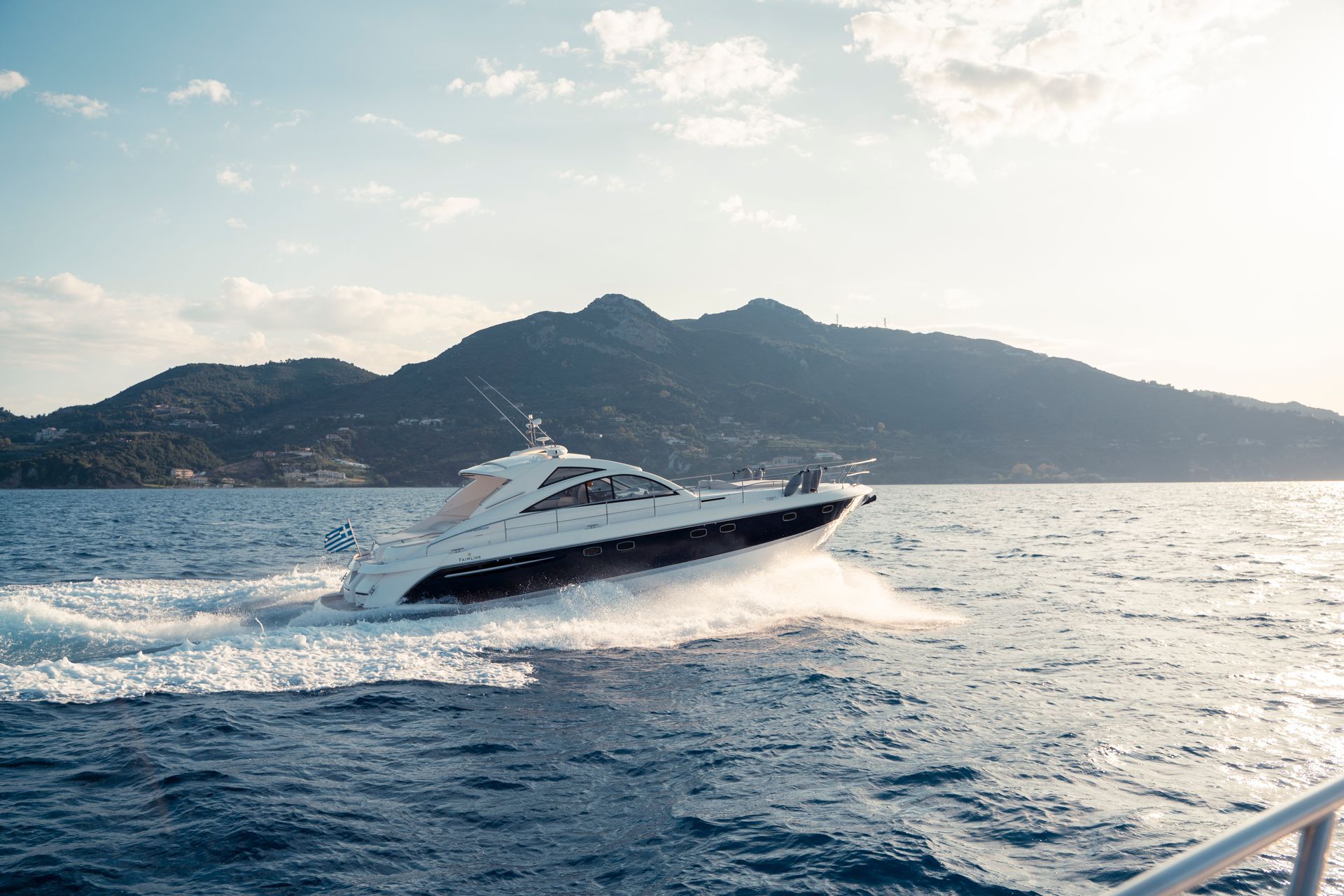 White speedboat skimming across blue sea near a mountainous coastline under a bright sky