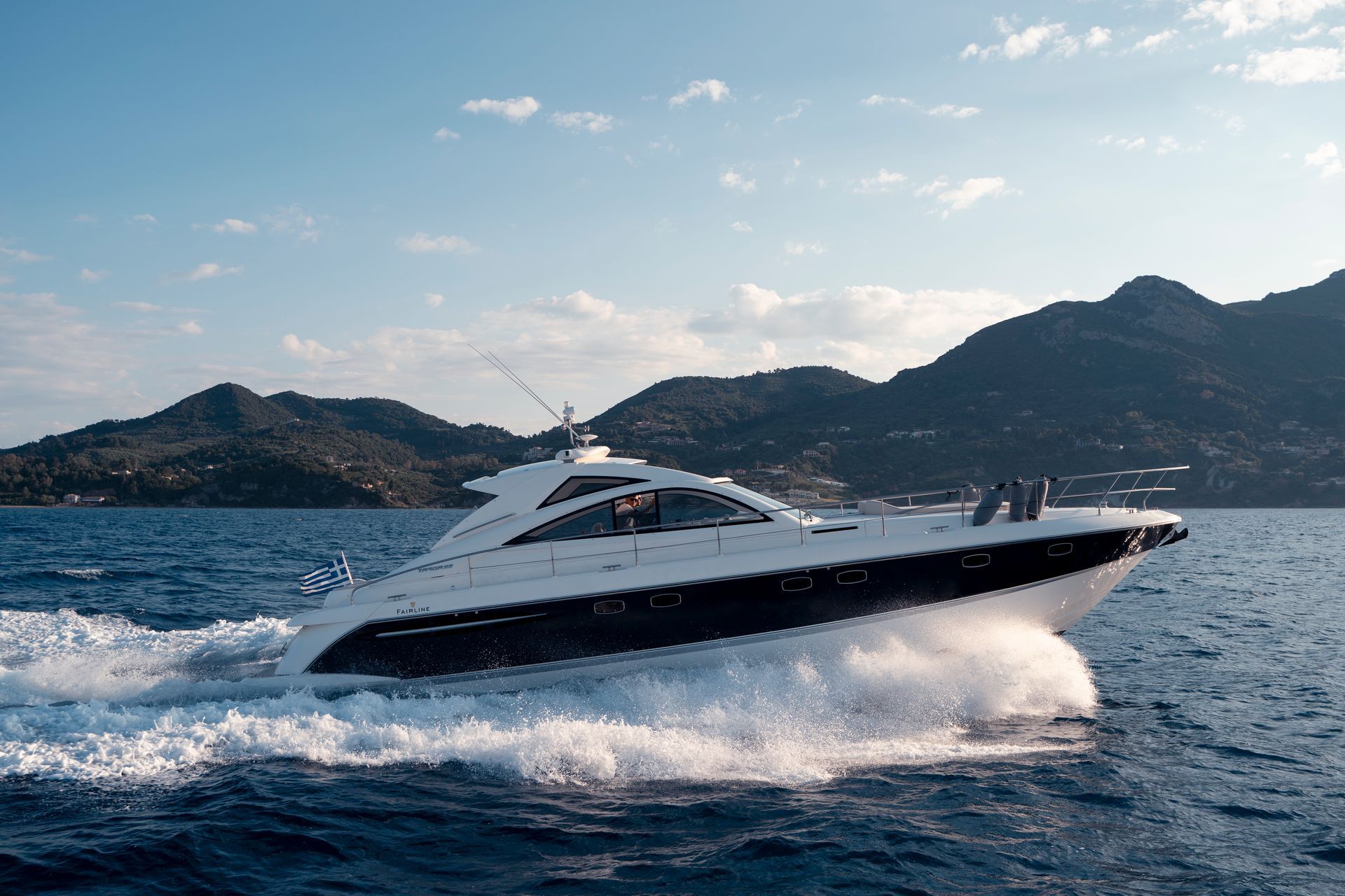 White yacht speeding across choppy blue water near mountainous coastline