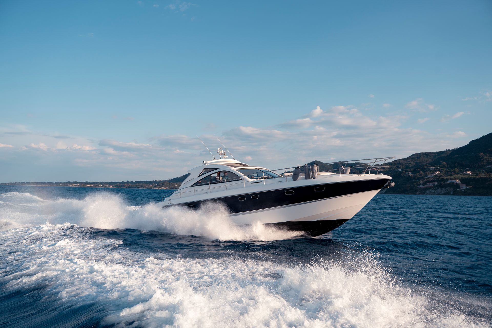 Luxury yacht speeding across choppy blue water near a coastal shoreline under a clear sky