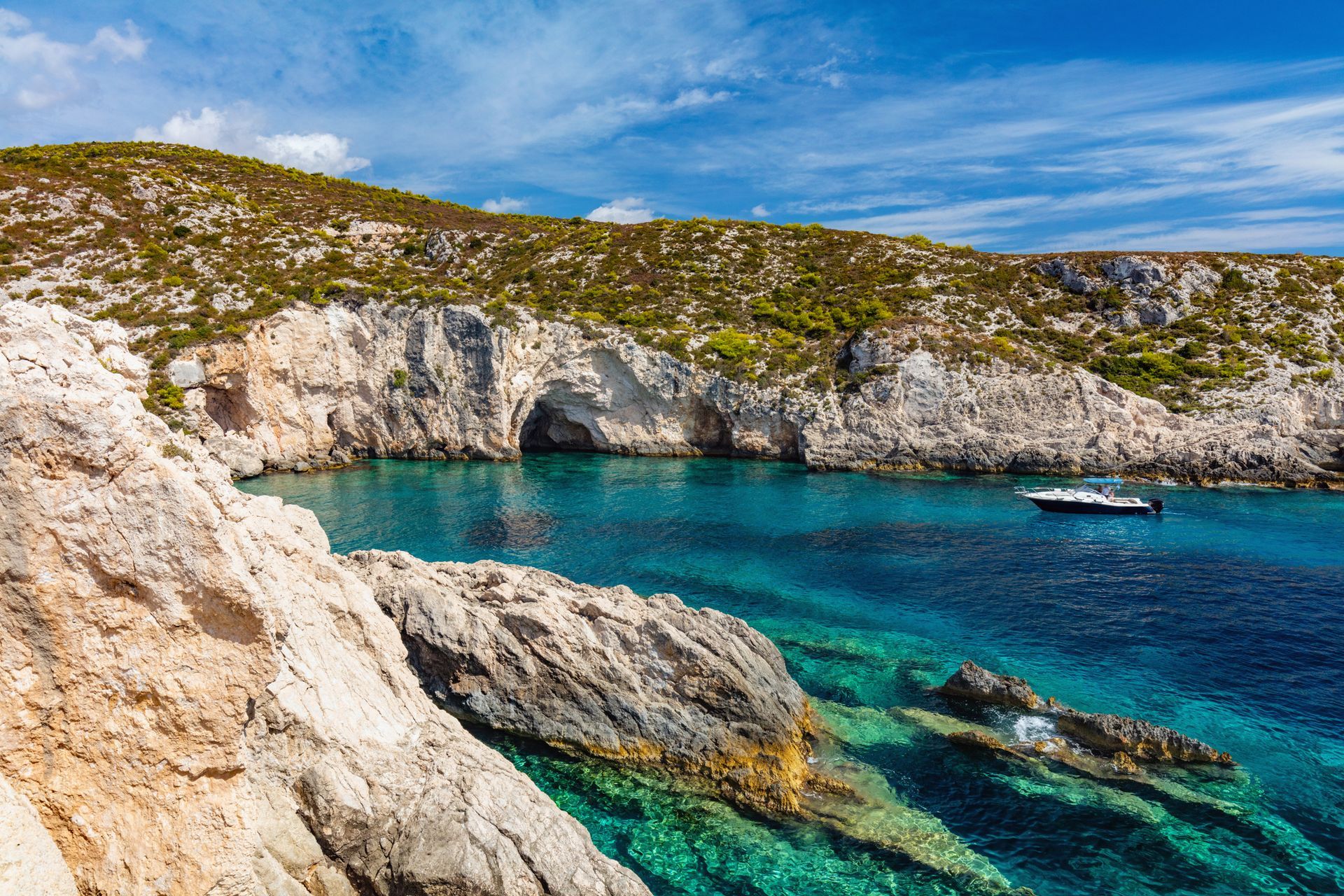 Rocky turquoise cove with white cliffs, clear blue water, and a small boat near the shore