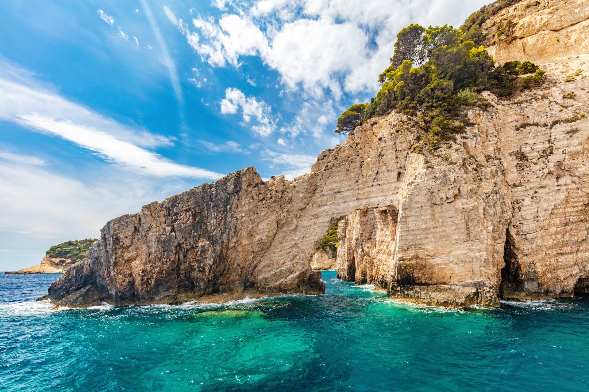 Rocky seaside cliffs with a natural arch above turquoise water under a bright blue sky